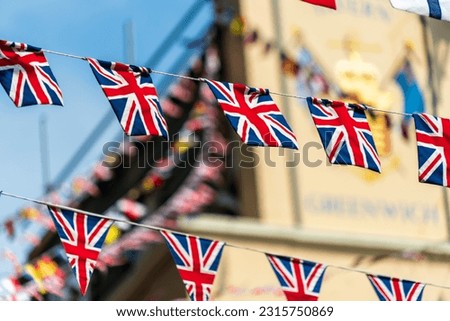 UK Union Jack flags decorate a Greenwich, London street above a traditional English pub. The decorative UK flags are colorful and create a festive atmosphere that English locals and tourists enjoy. 
