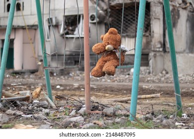 Ukraine, Borodyanka - 04.21.2022: A teddy bear without a paw on a broken swing against the background of a destroyed building, war. Consequences of Russian Attacks on Ukraine 