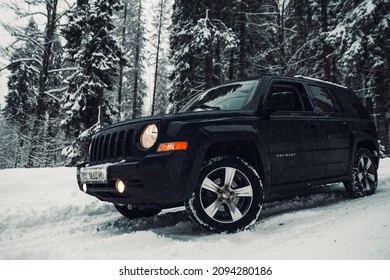 Ukraine, Carpathian Mountains. 11th Of December, 2021. View To The Front Of Dark 2015 Jeep Patriot Driving In The Mountains During Winter With Trees Covered In White Snow At The Background. 