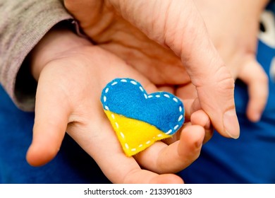 Ukraine flag theme. Heart shape pin badge made of  blue and yellow stuffed felt in child hand. Topical issues of war. Freedom fighters. Support of nations, unity