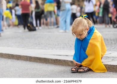 Ukraine girl flag on Support Rally in Europe. Sad Child wrapped in Ukraine flag misses in Rally In Support Of Ukraine.
