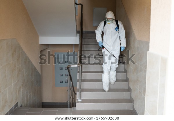 UKRAINE, KYIV - May 20, 2020: Man in a white\
protective suit and mask is sanitizing interior surfaces inside\
buildings while the coronavirus epidemic for infection prevention\
and control of\
epidemic.