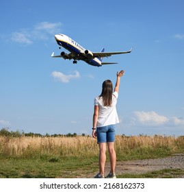 Ukraine, Lviv - September 14, 2021: Back View Of Woman Waving Hand To Landing Commercial Airplane In The Sky. Lifestyle And Travel Concept.