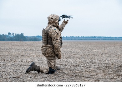 Ukrainian army soldier kneels in a field and launches a quadcopter into the sky. The soldier is dressed in military fatigues and wears a helmet with a face shield.