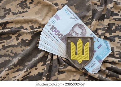 Ukrainian army symbol and bunch of hryvnia bills on military uniform. Payments to soldiers of the Ukrainian army, salaries to the military. War in Ukraine