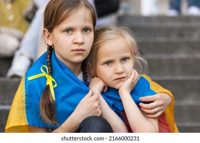 Ukrainian Children Refugee. Sad Migrant Children. Two frightened Girls wrapped in Ukraine Flag. Evacuation Kids from War Ukraine.