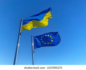 Ukrainian and European Union flags on flagpoles against blue sky - Shutterstock ID 2137095273