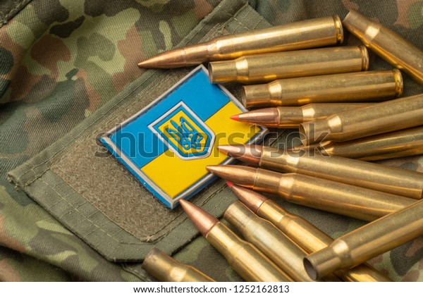 Ukrainian flag and coat of arms against\
camouflage and battle bullets. The concept of the Ukrainian defense\
army, highlight