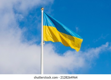 The Ukrainian flag on the flagpole is fluttering in the wind against a blue sky with clouds. Concept: Ukrainians' struggle for independence, the war between Ukraine and Russia.