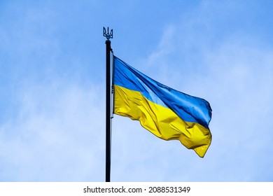 Ukrainian flag in the rays of the rising sun on a background of sky. Bicolor blue and yellow national flag of Ukraine on a flagpole and coat of arms of Ukraine trident. Official symbol of Ukraine