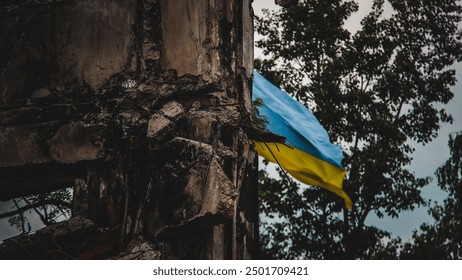 A Ukrainian flag waves in the background of war-torn ruins, captured with an artistic blur effect. The image symbolizes resilience amidst destruction during the war in Ukraine