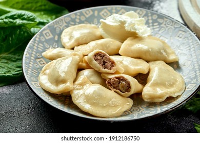 Ukrainian or Polish traditional dish - Pierogi or Varenyky (dumplings) stuffed with meat and sour cream. dark background. Close up, selective focus