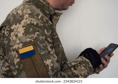 Ukrainian soldier in uniform with using smartphone. A banner of the Ukrainian flag on a soldier's pixel camouflage uniform. Ukrainian flag on chevron in blue and yellow colors.  - Powered by Shutterstock