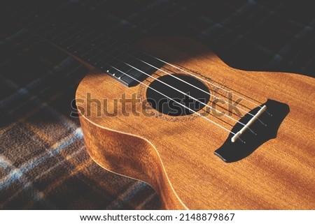 Ukulele body, soundhole, bridge and neck on brown checkered plaid. Musical instrument.