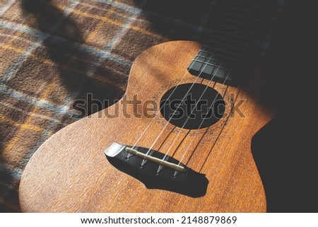 Ukulele body, soundhole, bridge and neck on brown checkered plaid. Musical instrument.