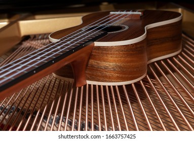 A ukulele made of solid wood lies on the strings of a grand piano