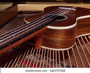 A ukulele made of solid wood lies on the strings of a grand piano