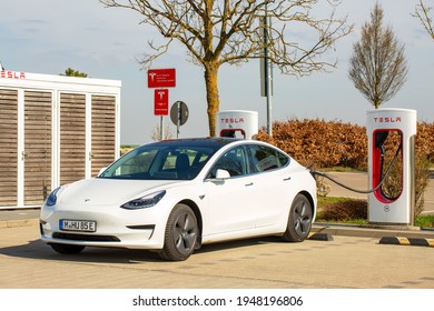 Ulm, Germany - April 01, 2021: White Tesla Model 3 plugged into Tesla super chargers in highway service area at Ulm, Germany.