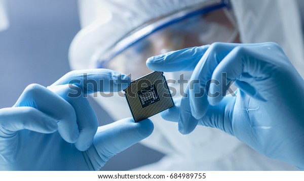 In Ultra Modern Electronic Manufacturing Factory\
Design Engineer in Sterile Coverall Holds Microchip with Gloves and\
Examines it.