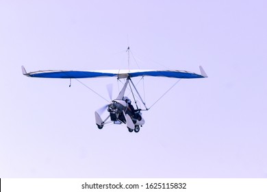 ultralight aircraft flies with people inside on a background of sky and clouds