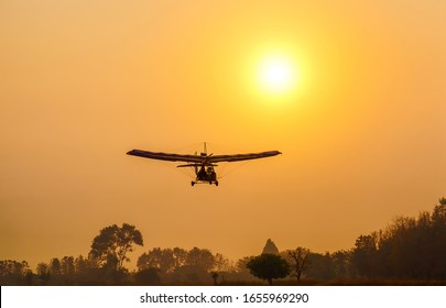 Ultralight trike flying with a pilot and a passenger against sunset sky, A microlight aircraft with two passengers with the sun
