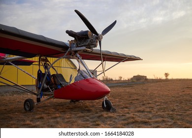 Ultralight two-seater airplane with a propeller stands on the airfield against the background of a hangar.