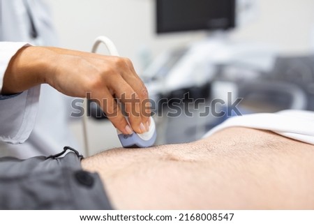 Ultrasound diagnosis of the stomach on the abdominal cavity of a man in the clinic, close-up view. The doctor runs an ultrasound sensor over the patient's male abdomen. Diagnostics of internal organs.