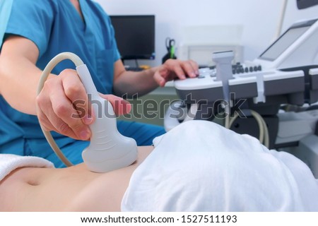 Ultrasound diagnostic of stomach on abdominal to woman in clinic, closeup. Doctor man runs ultrasound sensor over patient's girl tummy and looks at image on screen. Diagnosis of internal organs.