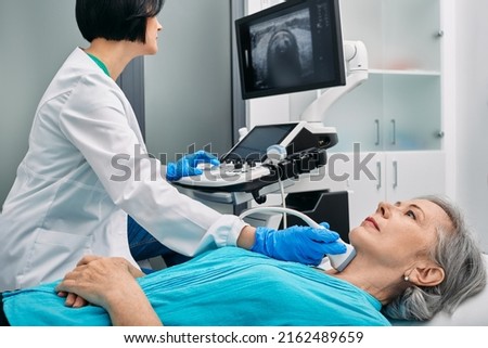 Ultrasound diagnostics of thyroid gland. Endocrinologist making ultrasonography to senior female patient at ultrasound office of medical clinic