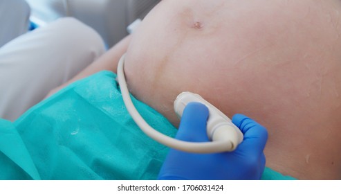 Ultrasound Examination In Doctors Office. Close Up Shot On The Ultrasound Transducer On Mothers Belly