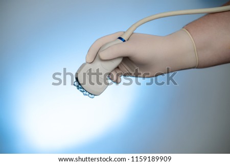 Ultrasound probe with sonographic gel held by hand high key blue light background