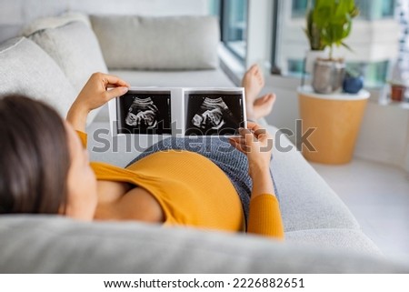 Ultrasound showing fetus. Pregnancy concept with pregnant woman looking at first photo of her baby, happily expecting the birth of her 1st child. First trimester pregnancy