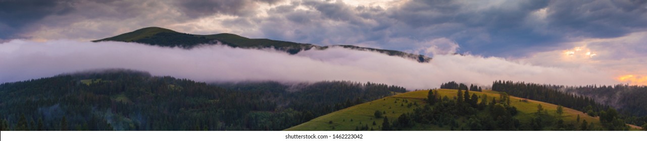 Ultra-wide panorama of foggy mountains after the rain at sunset moment. Dreamy beautiful mountains slopes, covered with spruce forest. Carpathian mountains. Ukraine.
