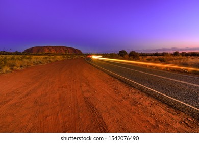 Uluru, Northern Territory, Australia - Aug 25, 2019: Car Light Trails Along The Road To Uluru At Night. The Sandstone Monolith Icon Of Australian Outback Red Centre In Uluru-Kata Tjuta National Park.