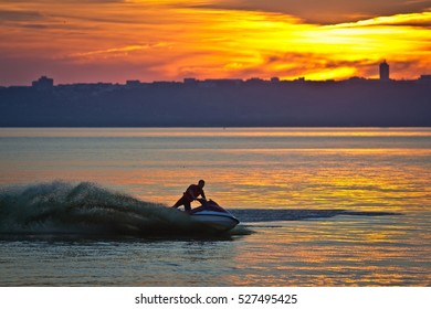 ULYANOVSK, RUSSIA - 20 JULY 2013. A man driving a jet ski on the Volga river at sunset. Blurred cityscape and sky in the background