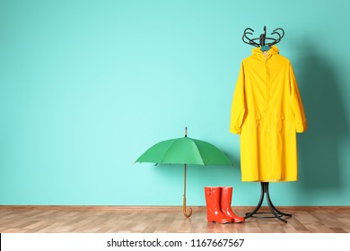 Umbrella, rain coat and boots near color wall with space for design