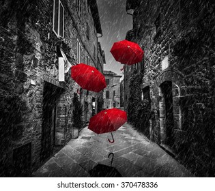 Umbrellas flying with wind and rain on dark narrow street in an old Italian town in Tuscany, Italy.. Black and white with red - Powered by Shutterstock