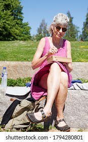 Umea, Norrland Sweden - July 8, 2020: Elderly Lady Sitting And Eating Lunch In The Sun