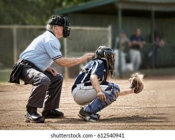 Umpire and catcher, just as ball hits catcher's mitt, dugout and players in background - Powered by Shutterstock