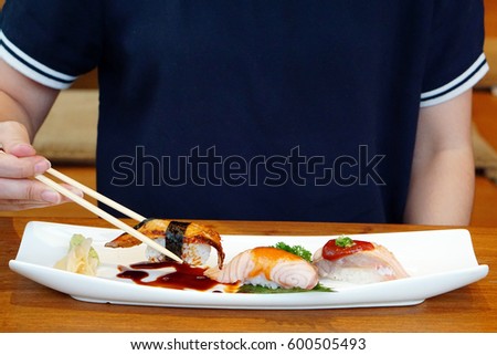 Unagi sushi and Salmon saikyo sushi on plate, Closeup a woman using chopstick hold unagi sushi (eel). Aburi style refers to nigiri sushi, the fish is partially grilled topside) and partially raw.
