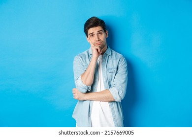 Unamused And Bored Man Looking Without Interest At Camera, Standing Against Bllue Background