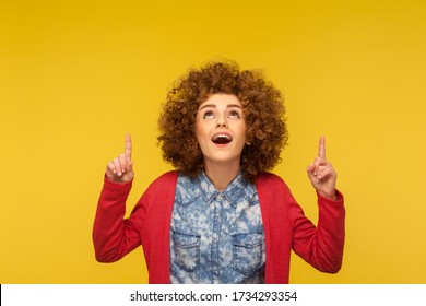 Unbelievable Advertise Here! Portrait Of Amazed Curly-haired Woman Pointing Up And Looking With Open Mouth, Shocked Expression, Showing Copy Space For Commercial Text. Indoor Studio Shot, Isolated