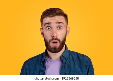 Unbelievable News. Portrait Of Bearded Young Guy Opening His Mouth And Eyes In Shock, Looking At Camera On Orange Studio Background. Thunderstruck Millennial Man Feeling Astonished