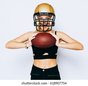Unbelievably beautiful athletic blonde girl in helmet on head posing in black outfit and holding ball. Sport. Match. American football. Copy. Paste. Indoor.
