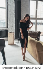 Unbelievably beautiful. Full length of attractive young woman in elegant black dress with a deep slit touching her hair while walking in the room