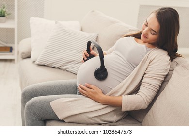 Unborn Baby Listening Music In Mother's Belly, Copy Space. Pregnant Woman Playing Classical Melody For Child By The Headphones. Therapy, Healthcare, Motherhood Concept