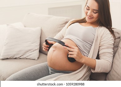 Unborn Baby Listening Music In Mother's Belly, Copy Space. Pregnant Woman Playing Classical Melody For Child By The Headphones. Therapy, Healthcare, Motherhood Concept