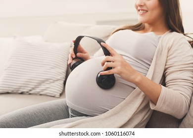 Unborn Baby Listening Music In Mother's Belly, Copy Space. Pregnant Woman Playing Classical Melody For Child By The Headphones. Therapy, Healthcare, Motherhood Concept