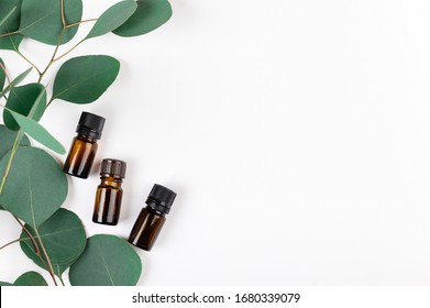 Unbranded amber glass bottles lying with green eucalyptus leaves. Cosmetic containers for natural medicine, essential and massage oil, aromatherapy products isolated on white. Copy space in right side