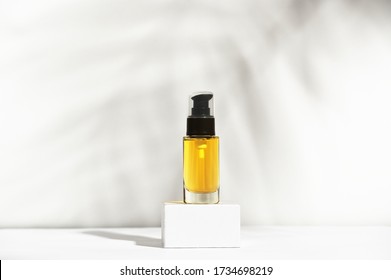 Unbranded Bottle With Dispenser On Pedestal. Transparent Glass Container With Oil For Body And Hair. Display Sample On Shadow Background. Mockup Style Design. Cosmetology And Beauty Concept